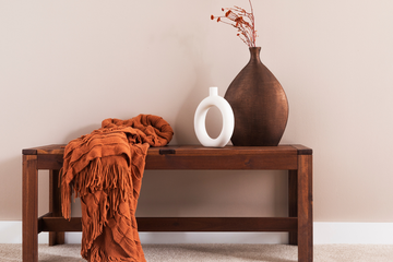 A timber bench with an orange throw blanket and decorative vases.